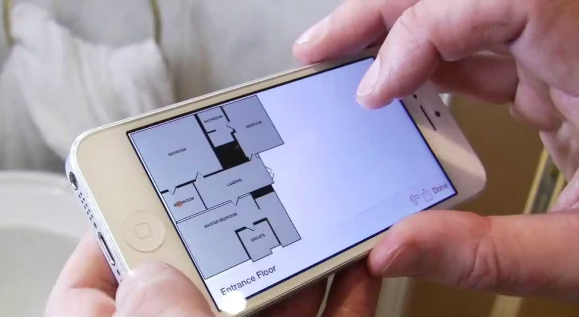 A person holds an iPhone displaying a detailed floor plan
