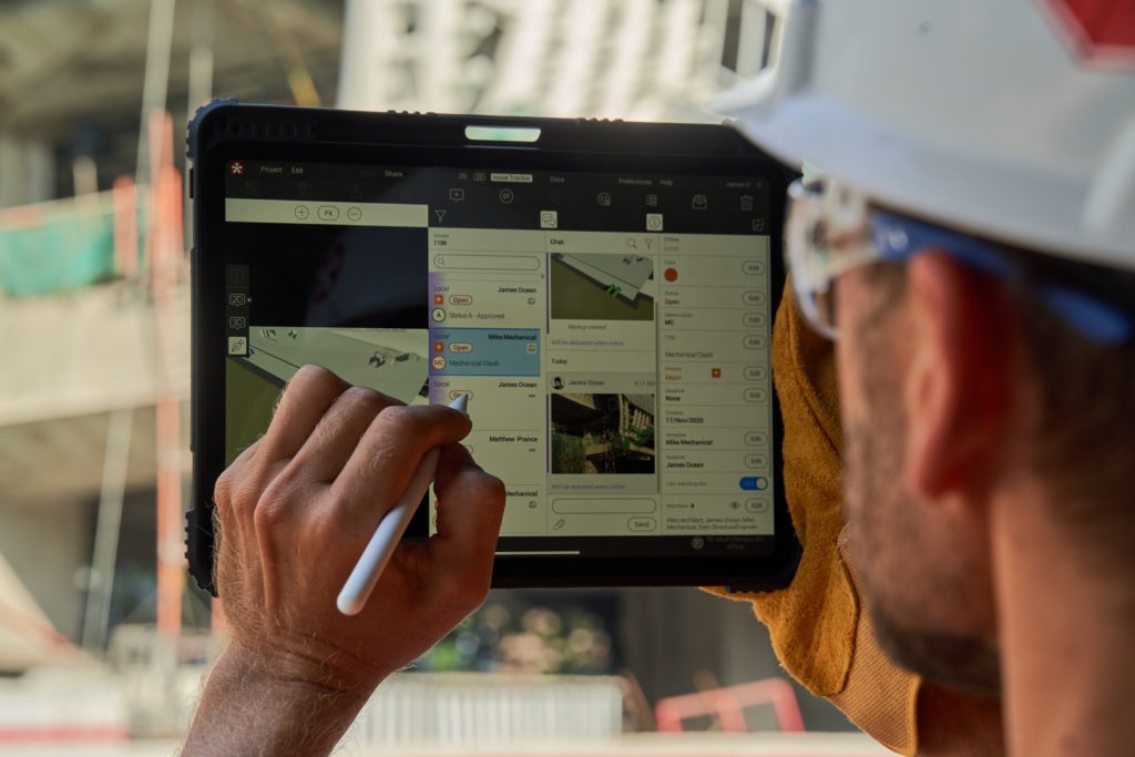 A man wearing a hard hat is focused on using an iPad at a construction site