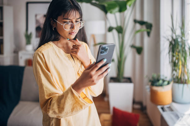 A woman with glasses and a yellow shirt looking at her phone