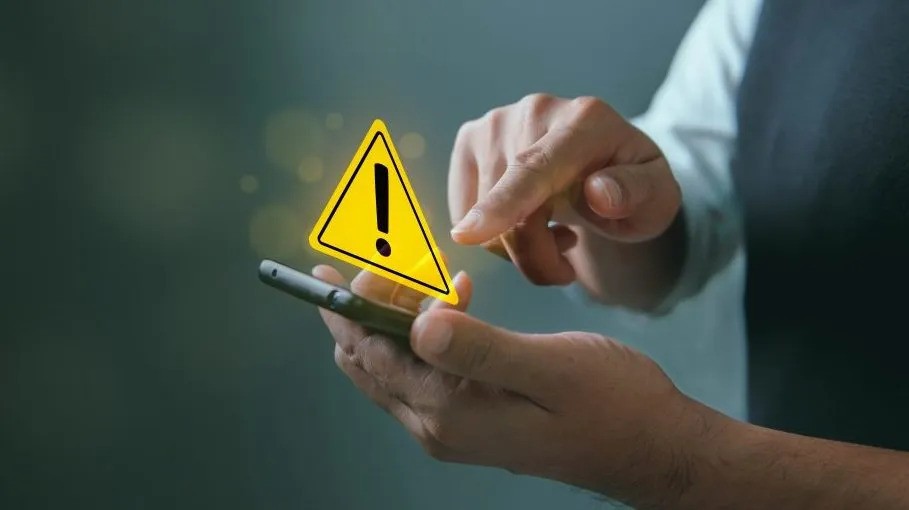 A man holds a smartphone displaying a yellow caution sign