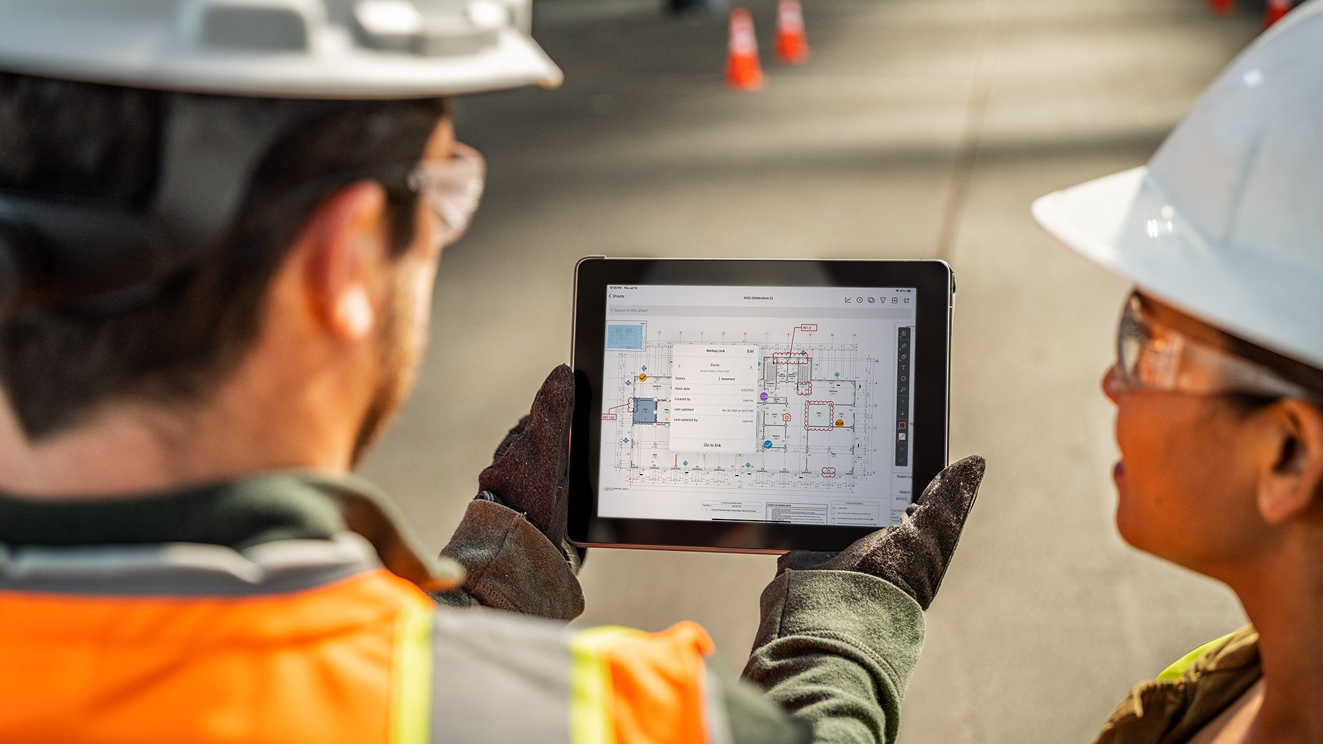 Two individuals in hard hats are holding a tablet computer